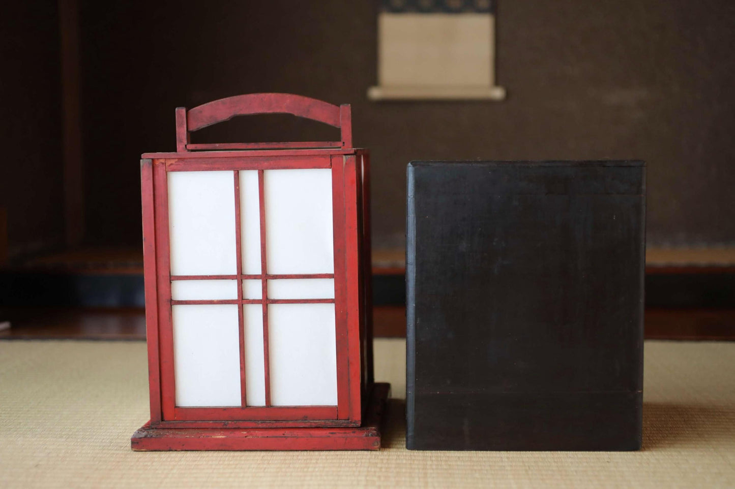 a red lantern with white panels and a black box placed on a beige surface.