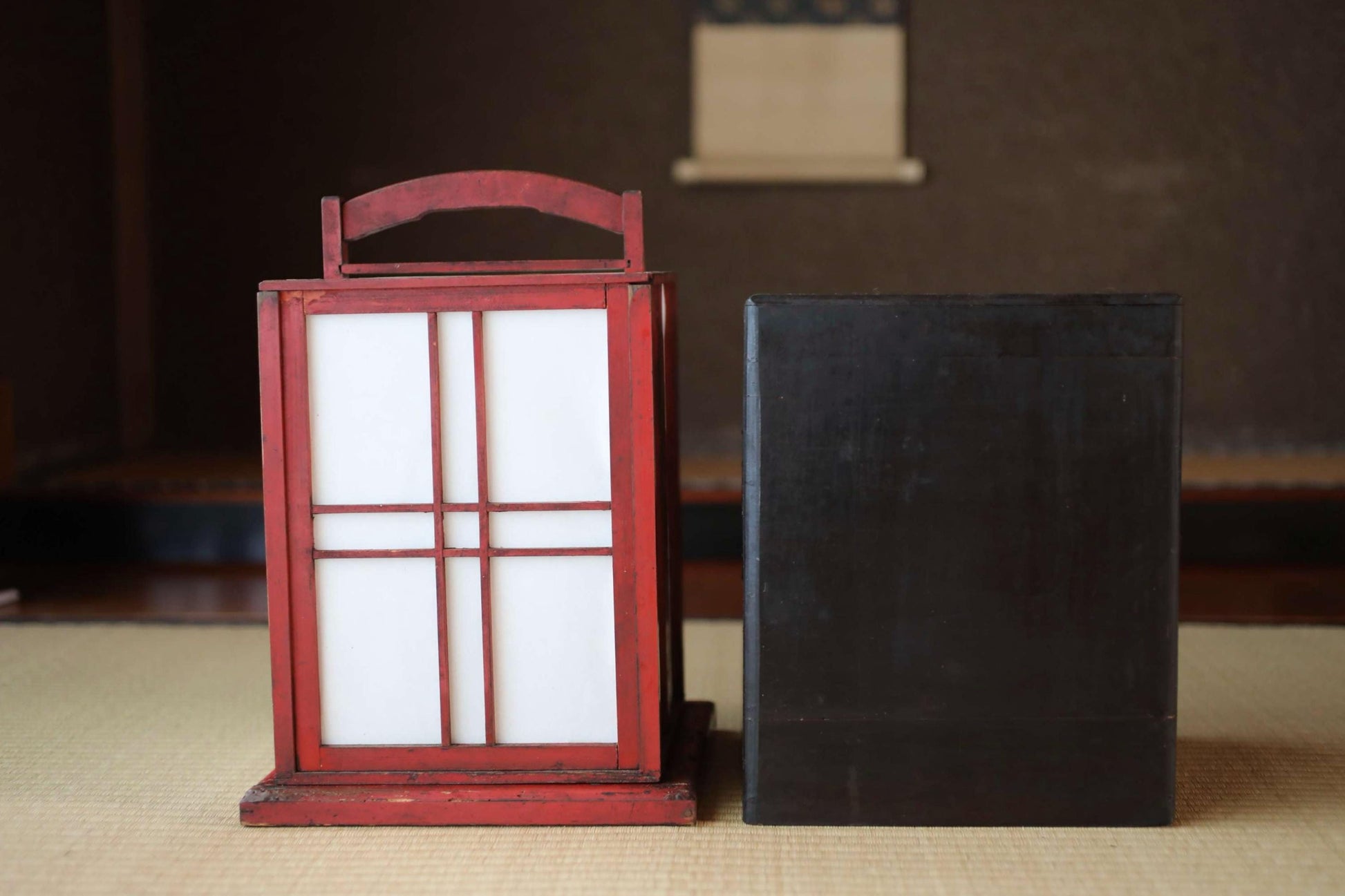 a red lantern with white panels and a black box placed on a beige surface.