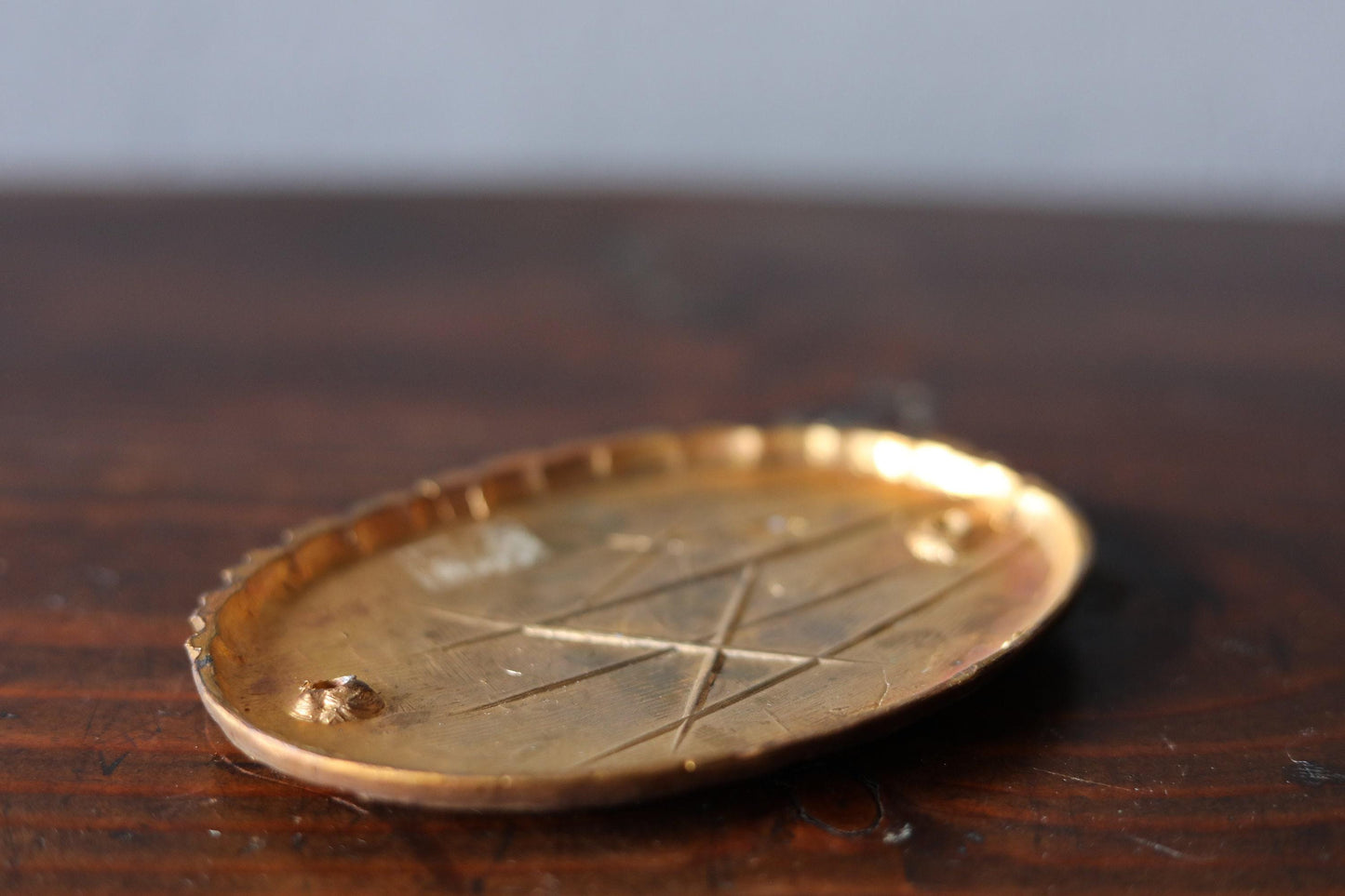 A close-up image of a golden, oval-shaped object with a pattern of lines on its surface, resting on a wooden surface.