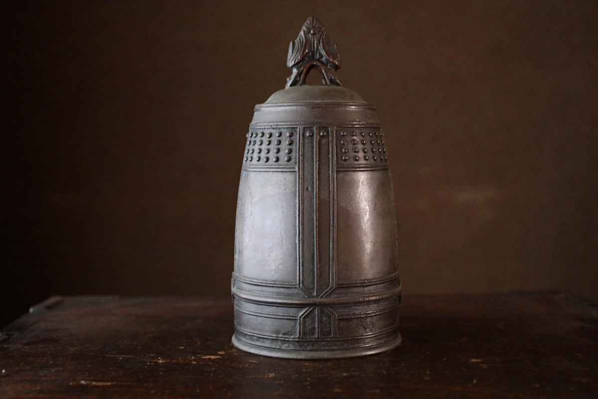 A metal bell with a decorative design on top, sitting on a wooden surface.