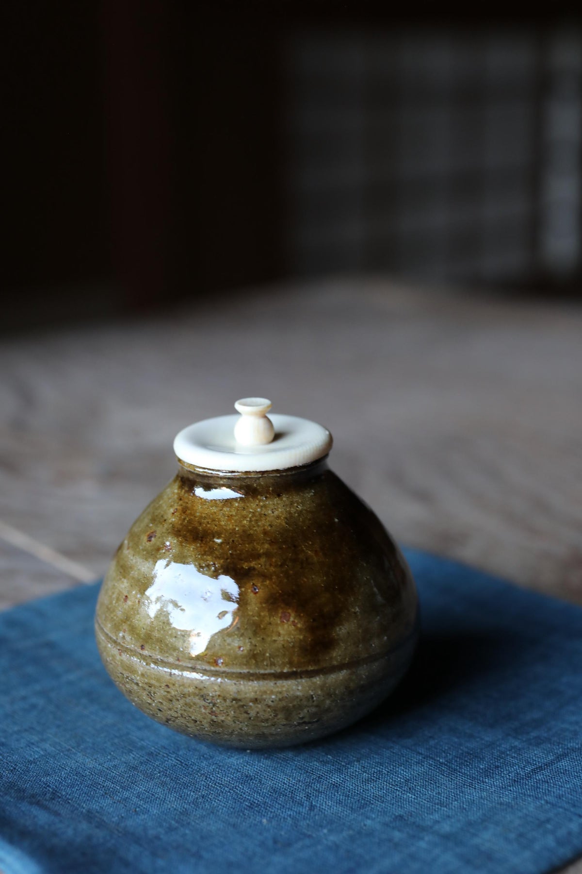 A ceramic jar with a white lid sits on a blue cloth, with a blurred background.