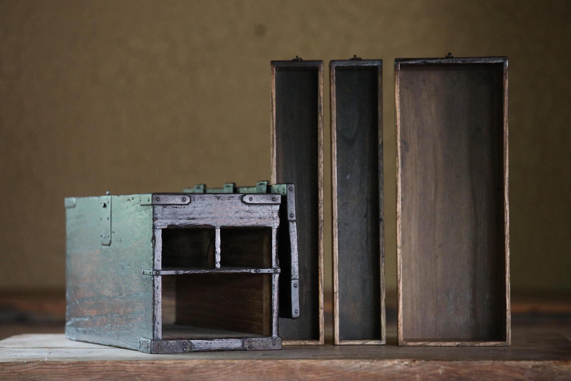 a collection of old, wooden boxes and a green metal box on a wooden surface.
