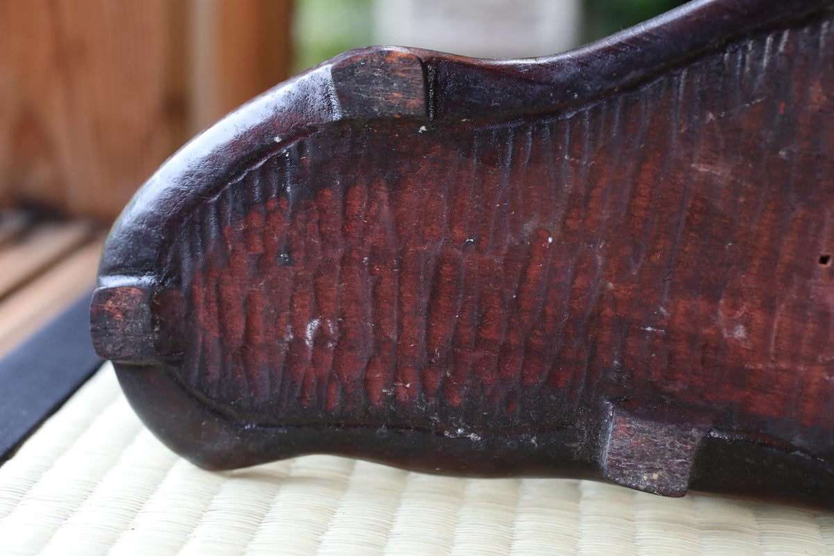 a close-up view of a dark wooden object, possibly a piece of furniture or a decorative item, with a textured surface and a dark brown color.