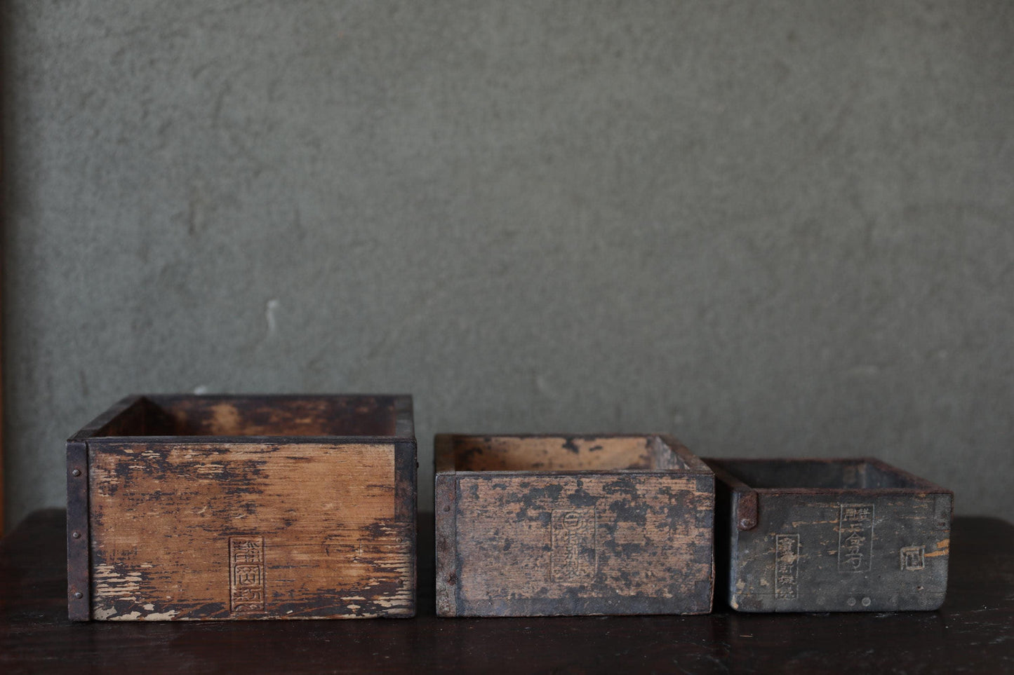 Three old, weathered wooden boxes sit on a dark surface against a gray background.
