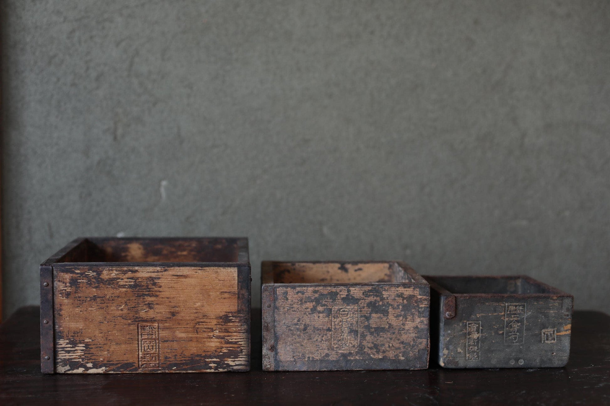 Three old, weathered wooden boxes sit on a dark surface against a gray background.
