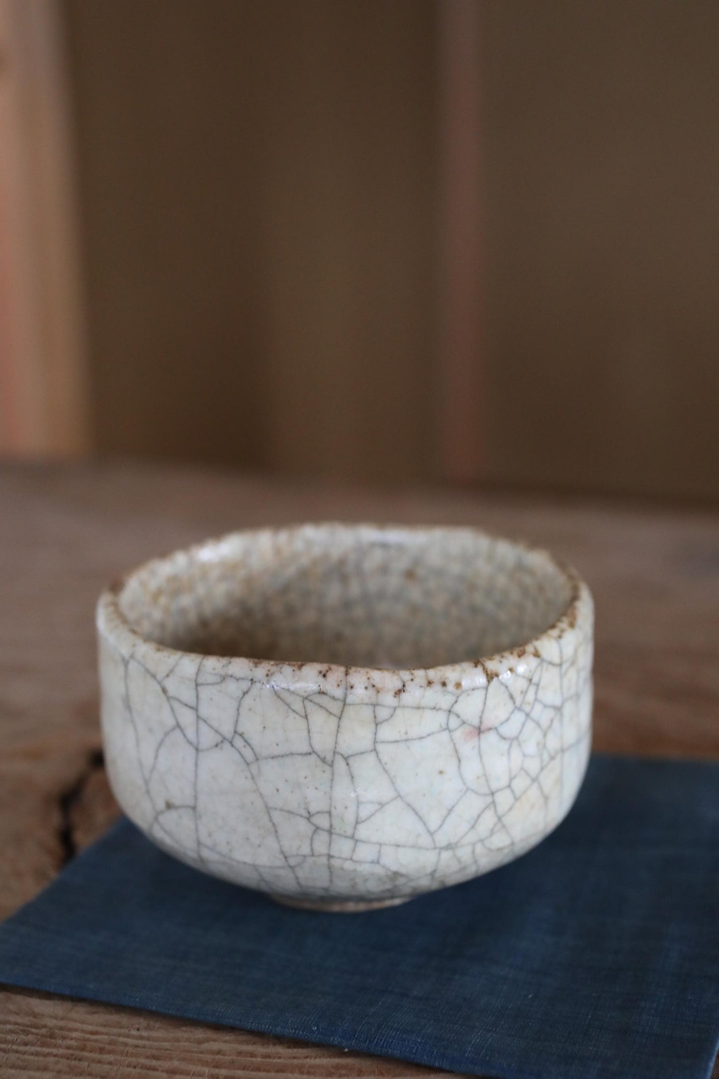 A white ceramic bowl with a cracked texture sits on a blue cloth on a wooden surface.