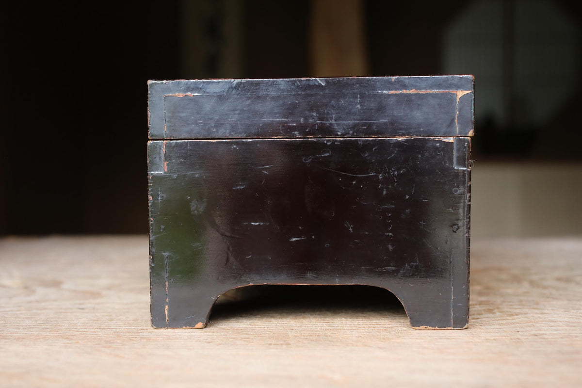 A dark wooden box with a visible crack on the top surface, sitting on a wooden surface.