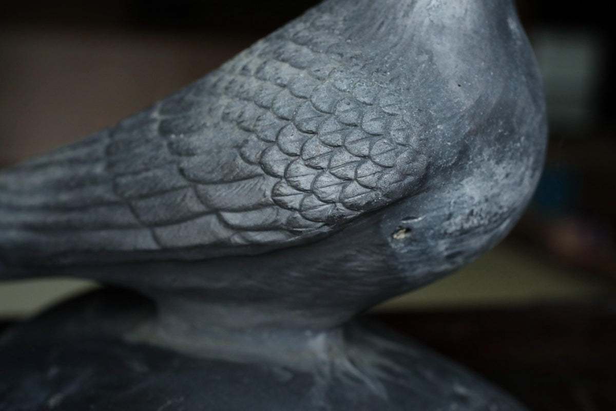 A close-up view of a bird statue, likely made of metal or stone, with intricate details and a textured surface.