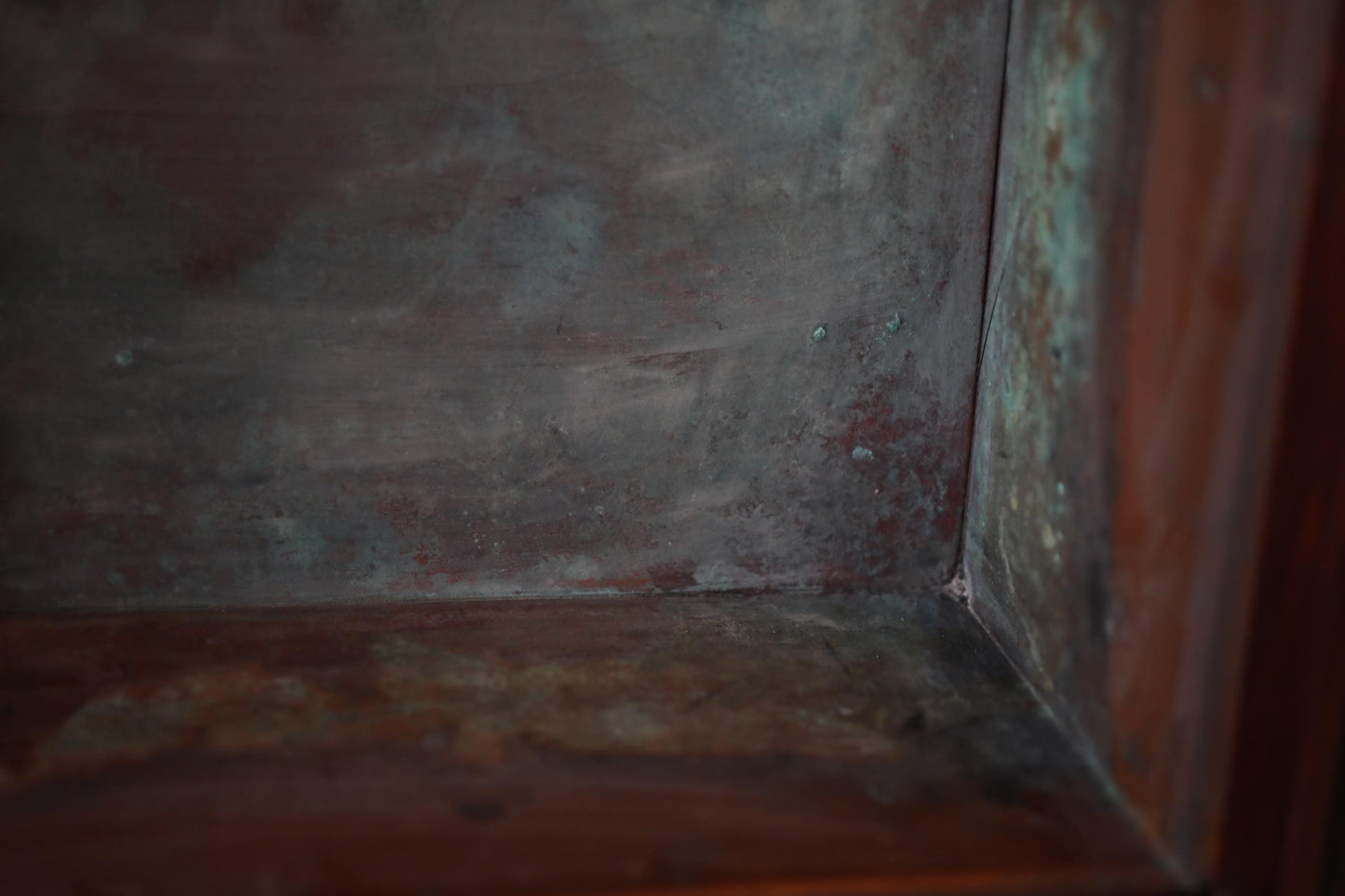 a close-up view of a metal surface with a reddish-brown hue, possibly rust or patina, and a few small holes or specks scattered across the surface.