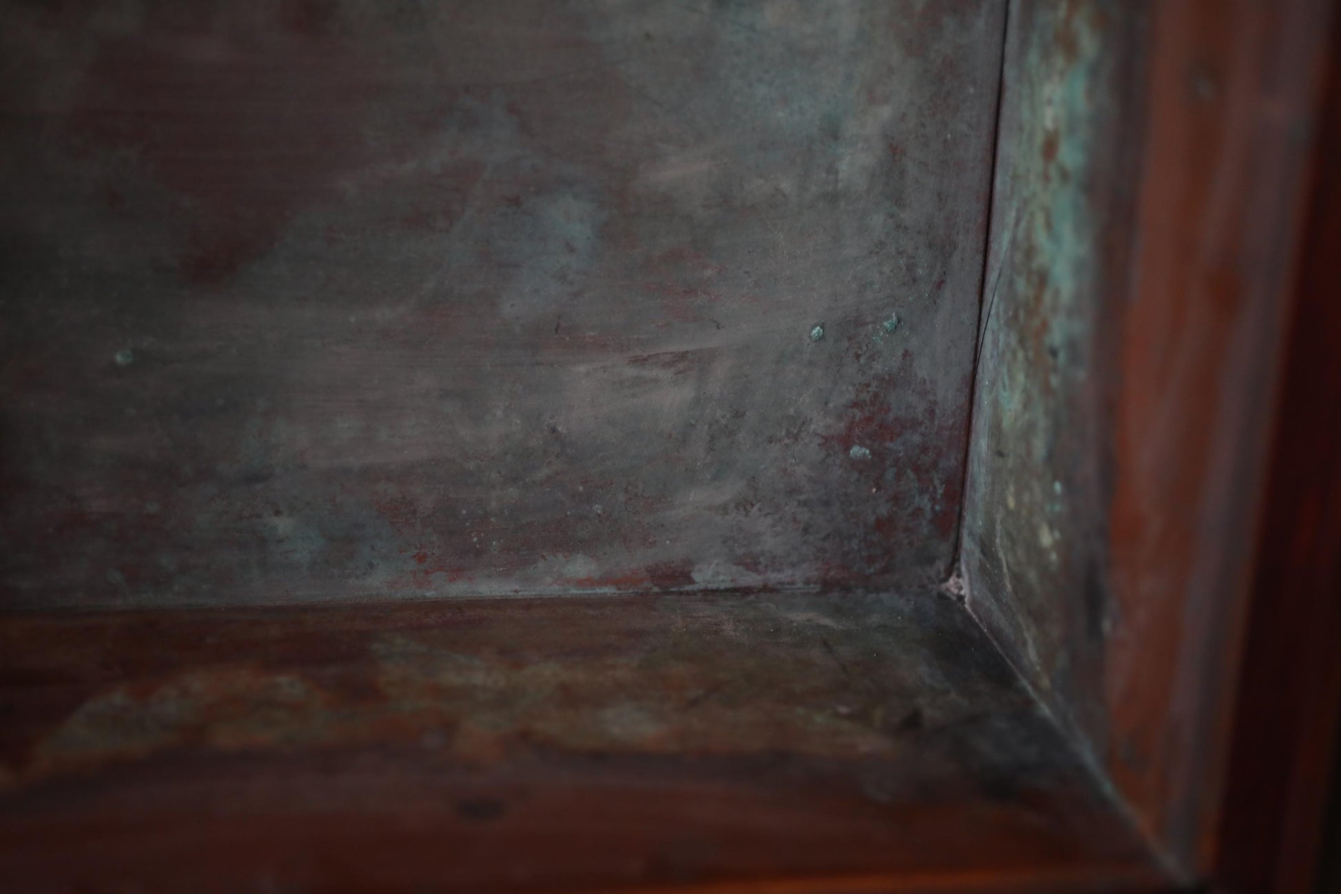 a close-up view of a metal surface with a reddish-brown hue, possibly rust or patina, and a few small holes or specks scattered across the surface.