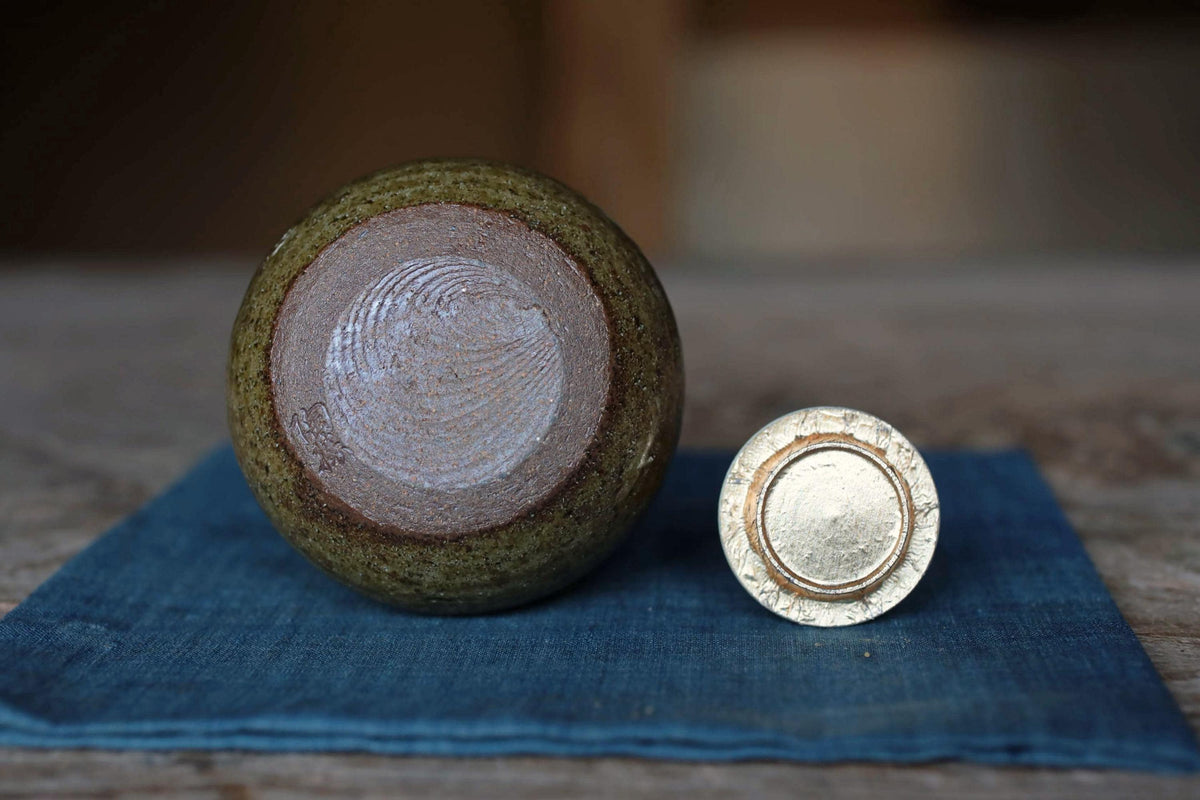 a green ceramic object with a white design on it, placed on a blue cloth on a wooden surface.