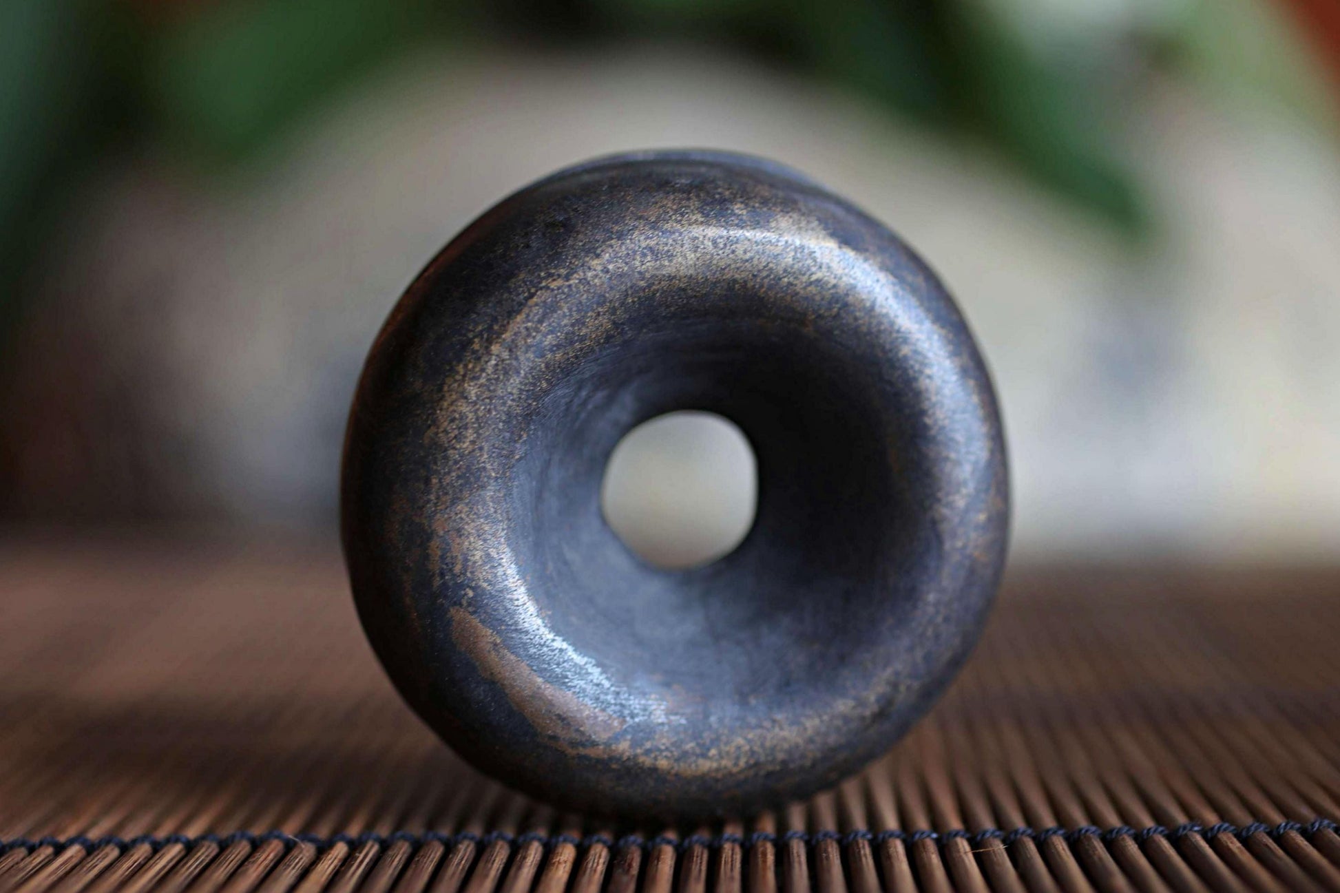 A close-up image of a dark, textured metal object with a hole in the center, resting on a bamboo mat.