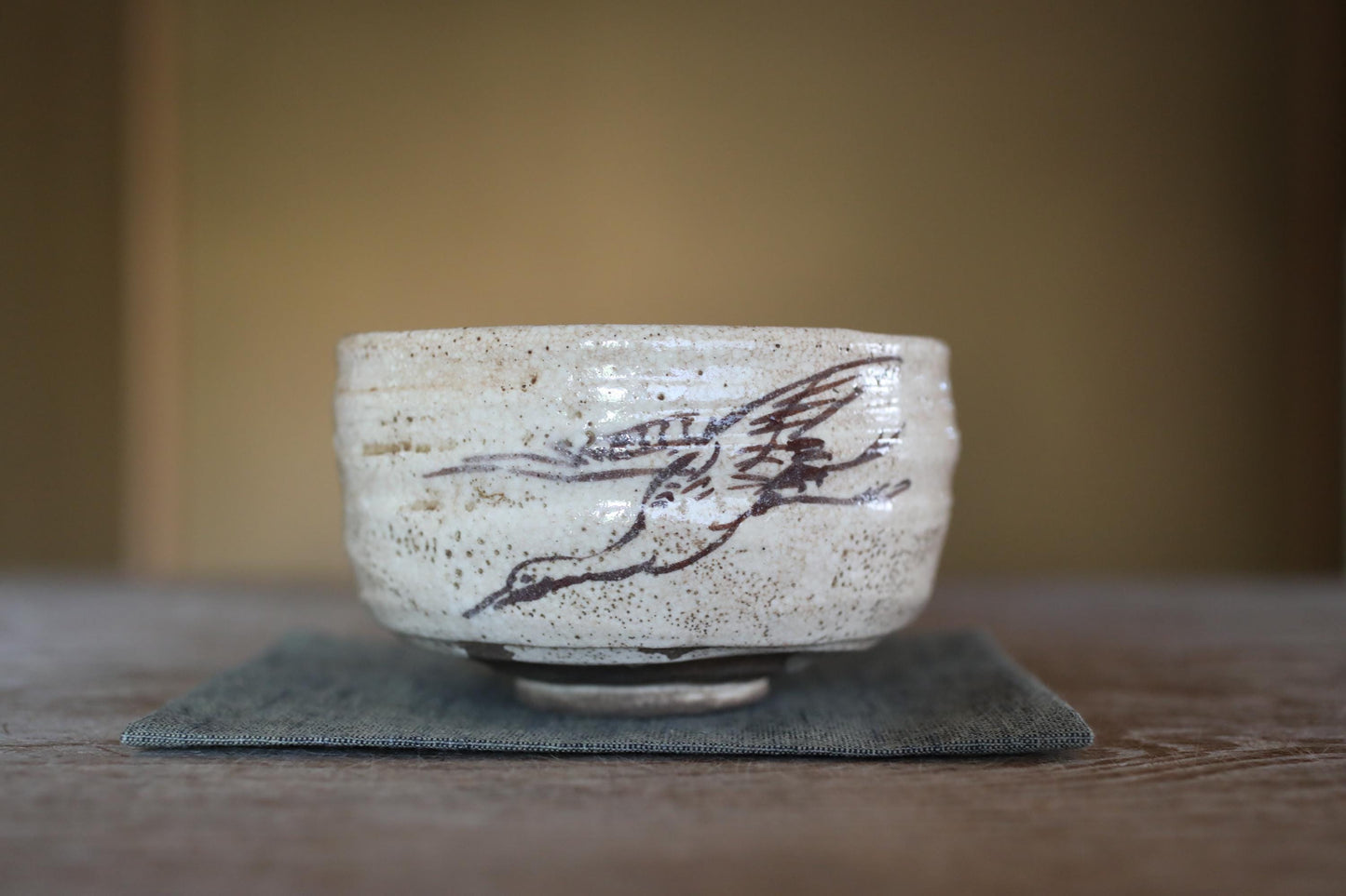 A ceramic bowl with a bird design on it, placed on a gray cloth on a wooden surface.