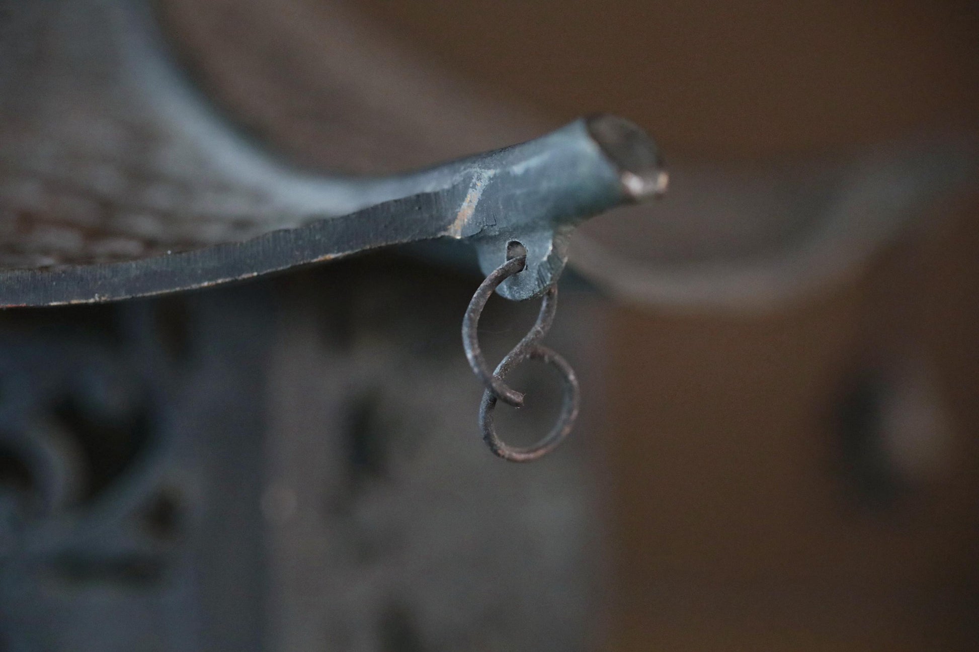 A close-up view of a metal hook or bracket attached to a curved metal structure, with a blurred background.
