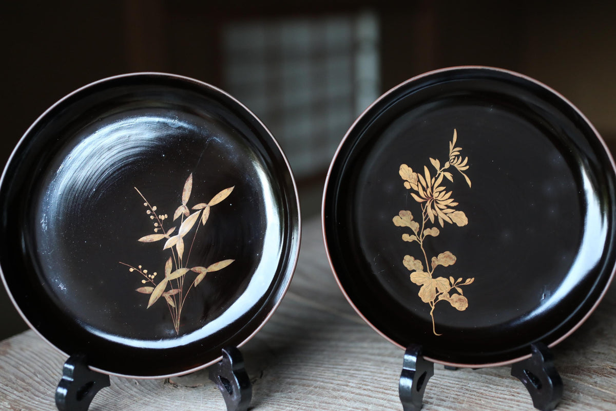 two black plates with gold floral designs, placed on a wooden surface.