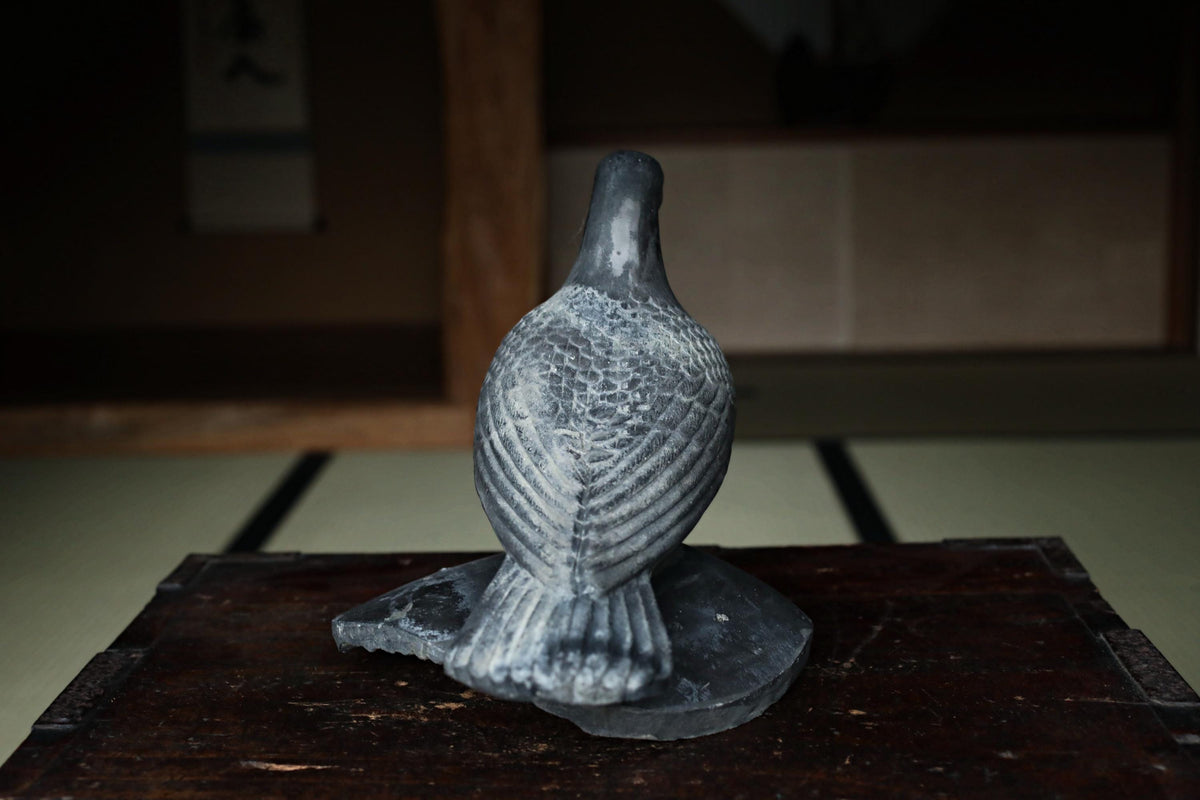 A gray stone statue of a bird, possibly a dove, sitting on a wooden surface.