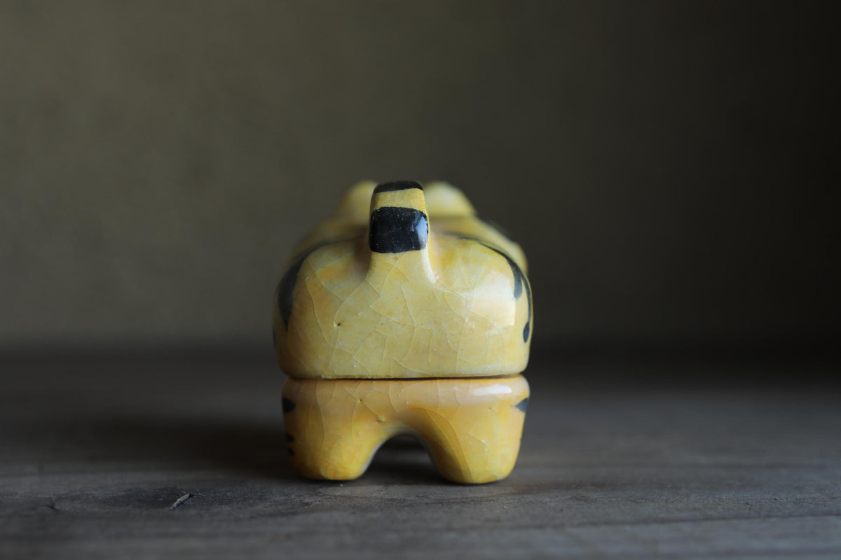 A small, yellow ceramic figurine with black accents is sitting on a wooden surface.