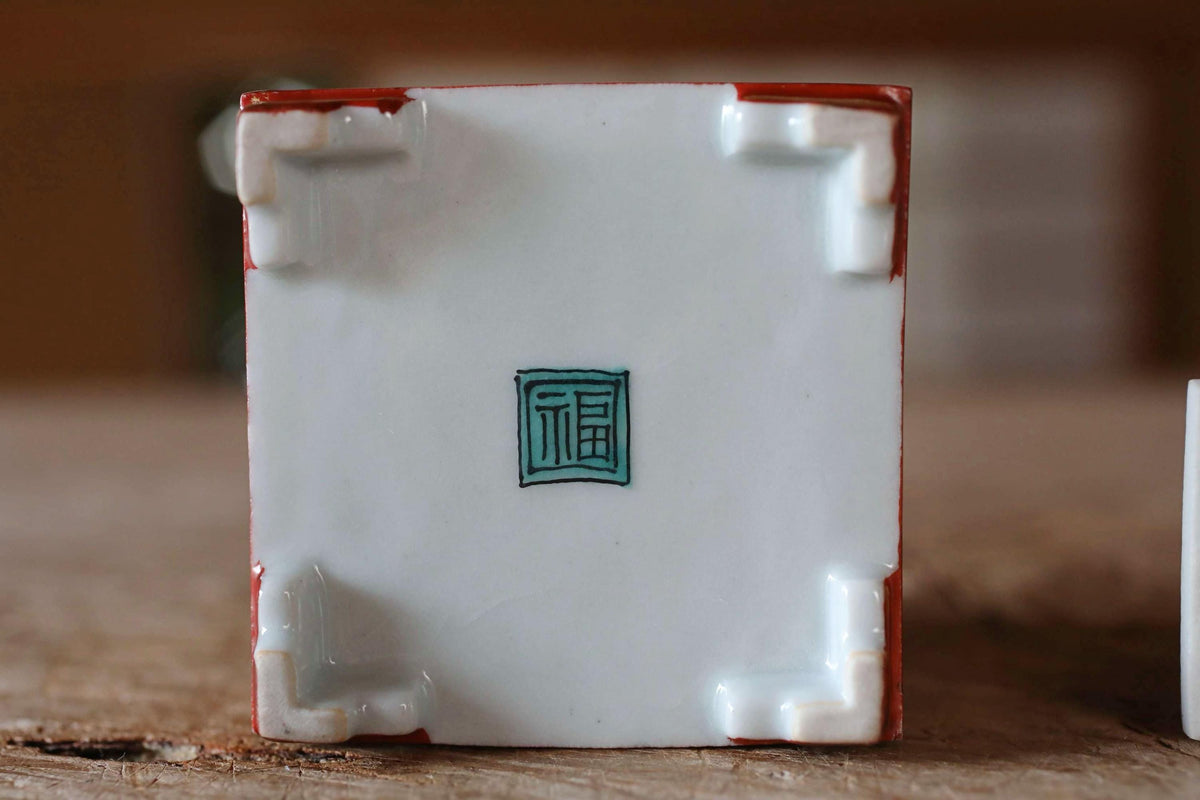 A square ceramic object with a red border and a green square design in the center, placed on a wooden surface.