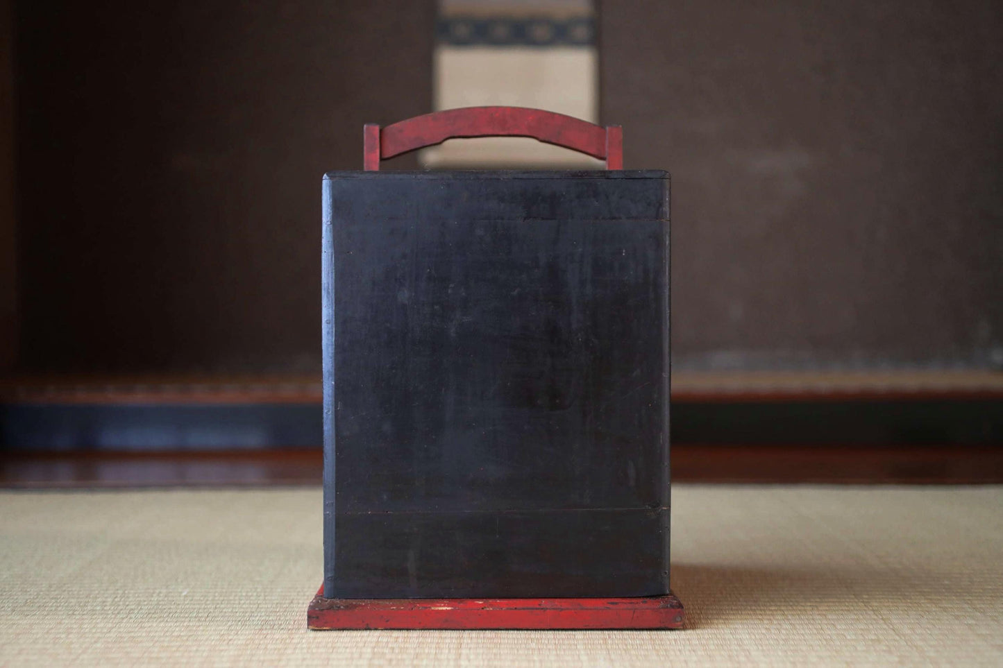 A black rectangular object with a red handle, placed on a beige surface.