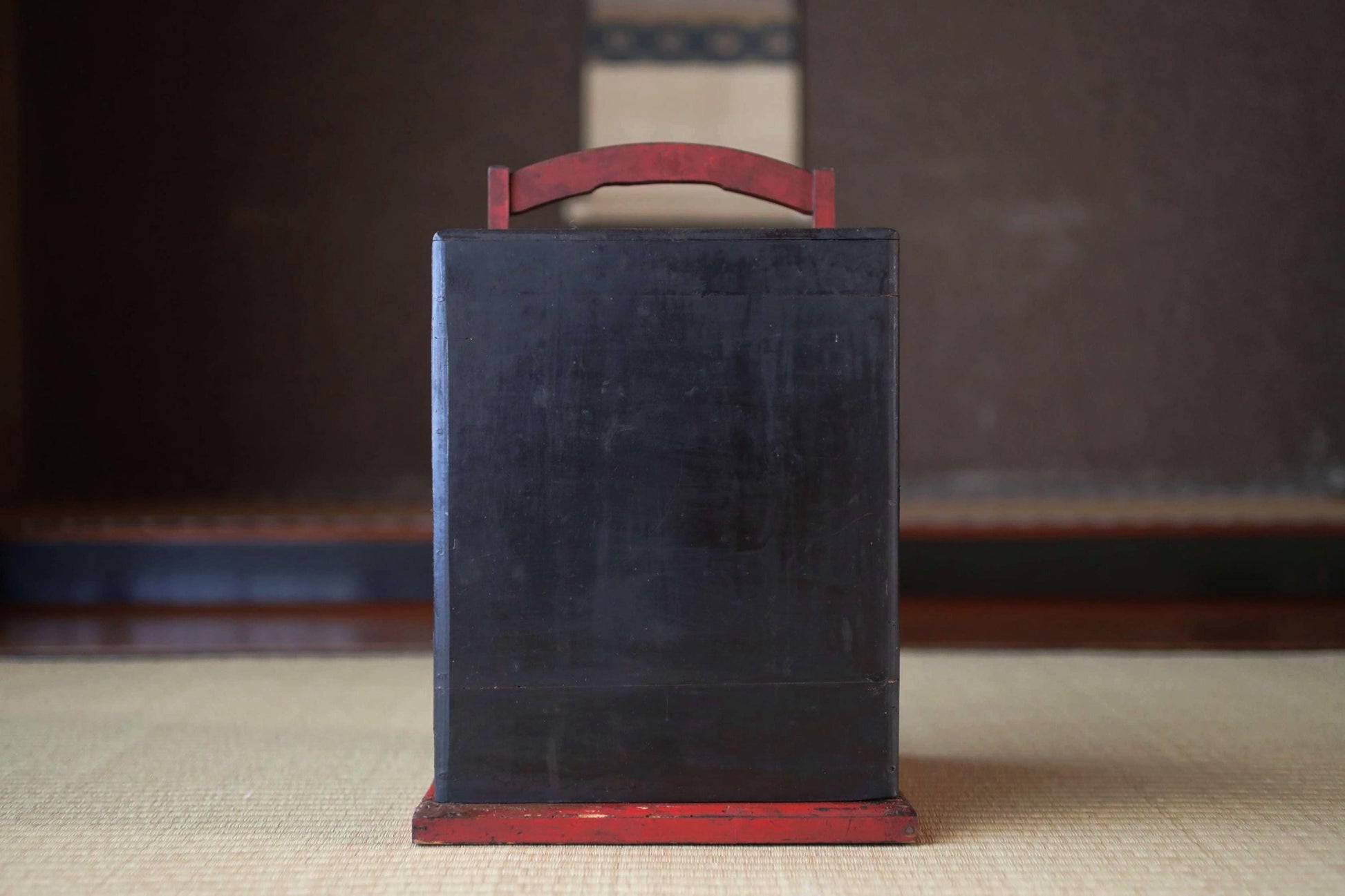 A black rectangular object with a red handle, placed on a beige surface.