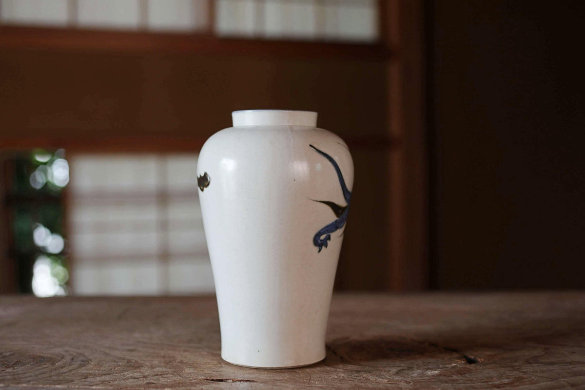 A white ceramic vase with a blue bird design on it, placed on a wooden surface.