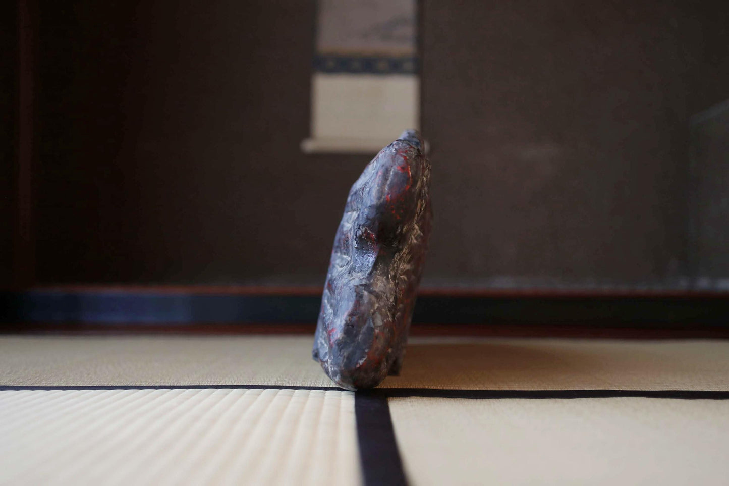 A dark, textured object resembling a rock or stone is positioned on a white surface, with a black and white patterned background.