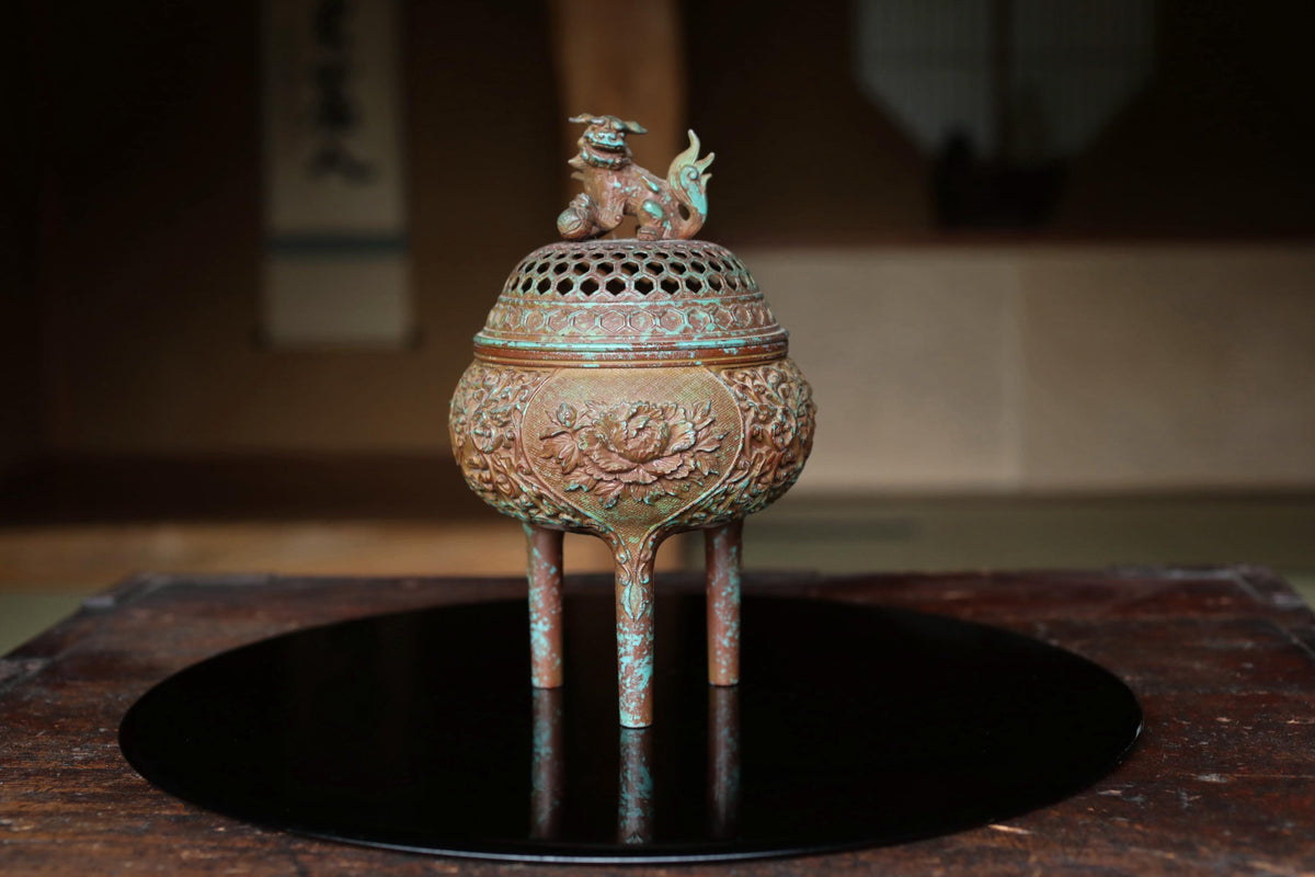 An ornate bronze incense burner with a dragon figure on top, placed on a black circular tray.