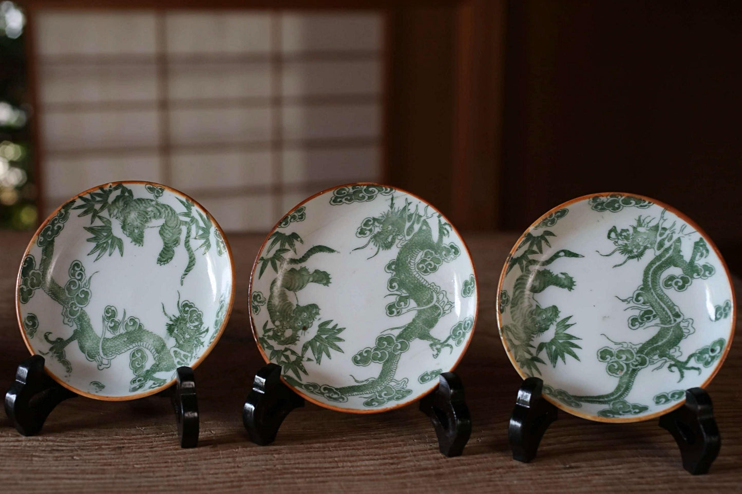 Three ornate plates with green dragon designs are displayed on a wooden surface.