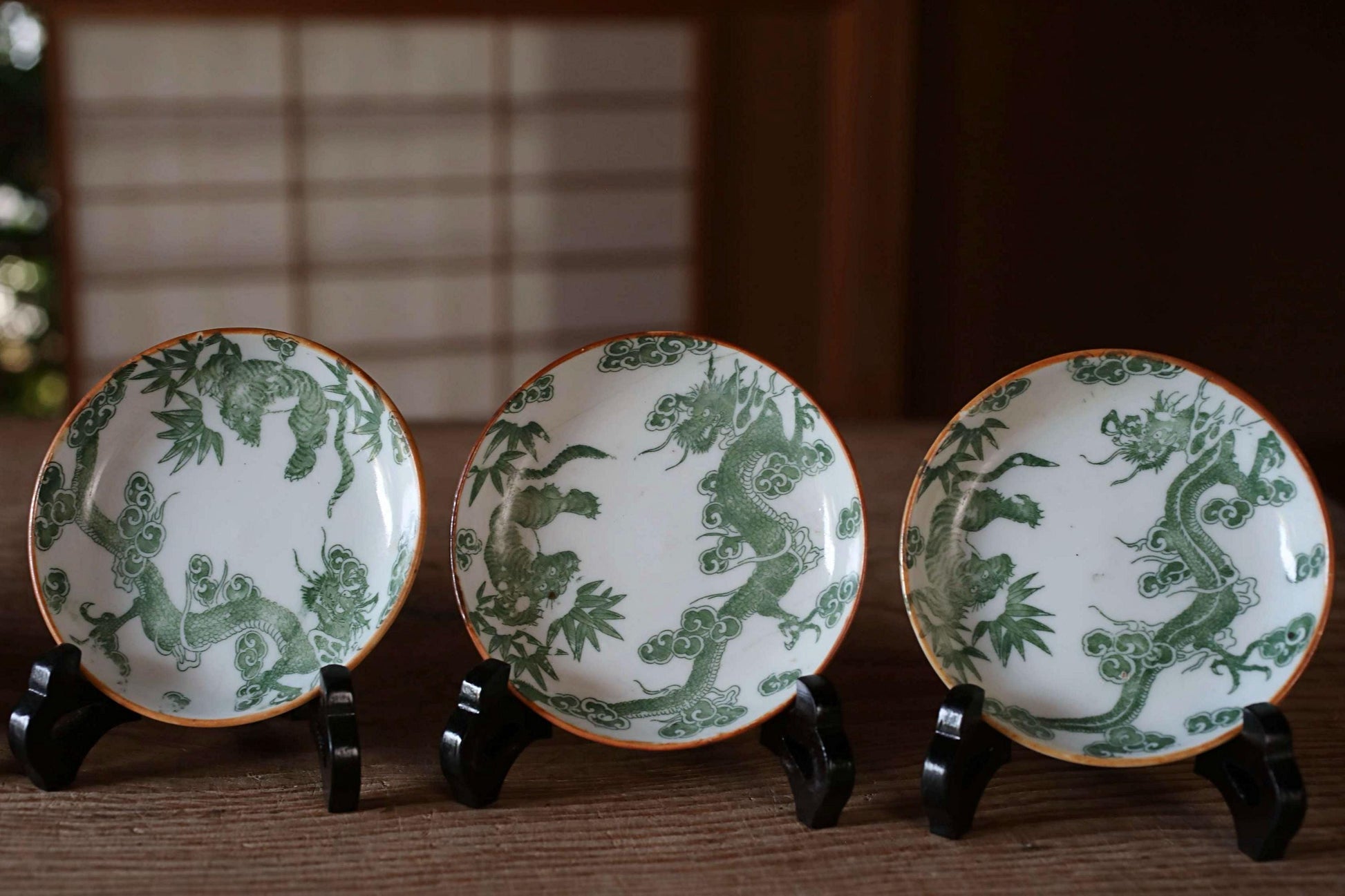 Three ornate plates with green dragon designs are displayed on a wooden surface.