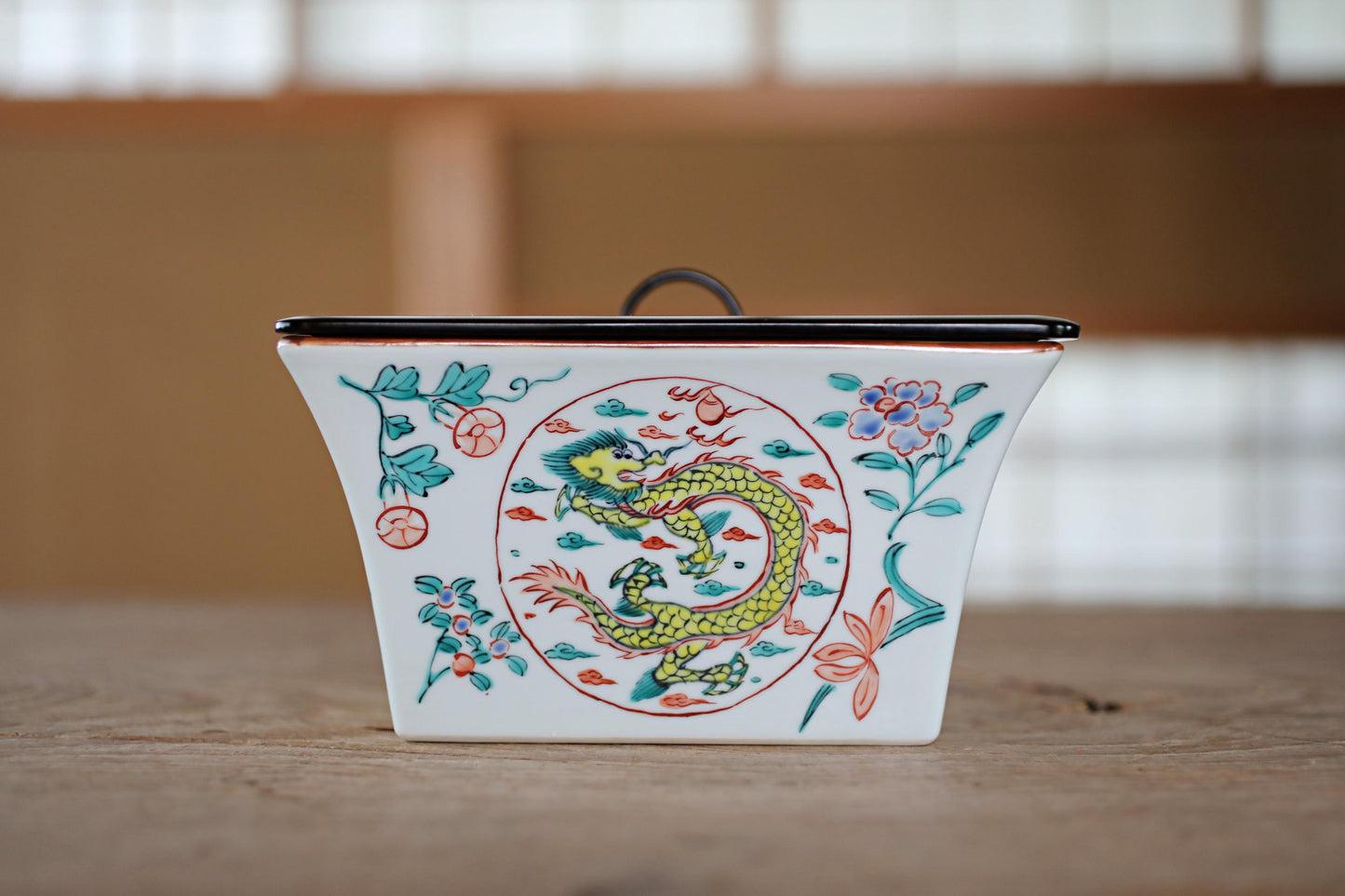 A ceramic container with a dragon design on it, placed on a wooden surface.