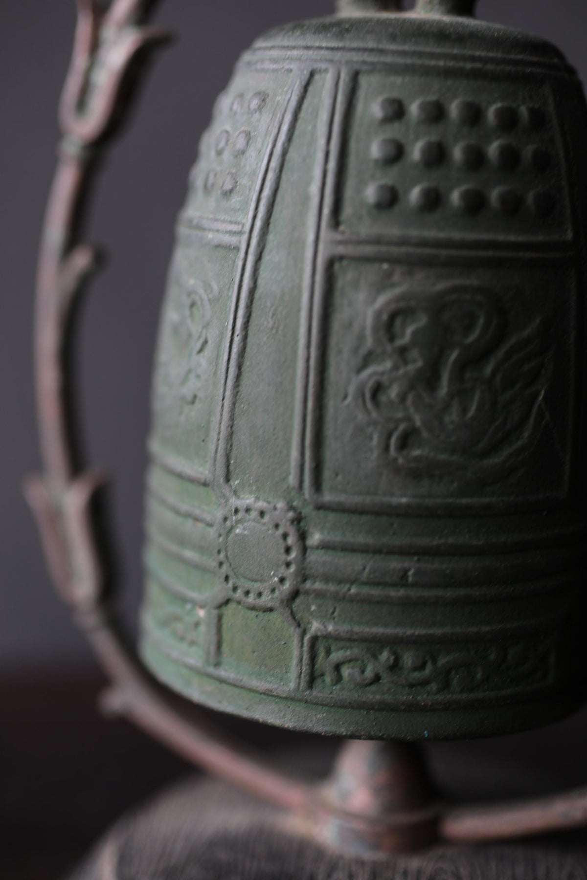 A close-up image of a green metal bell with intricate designs and patterns on its surface.