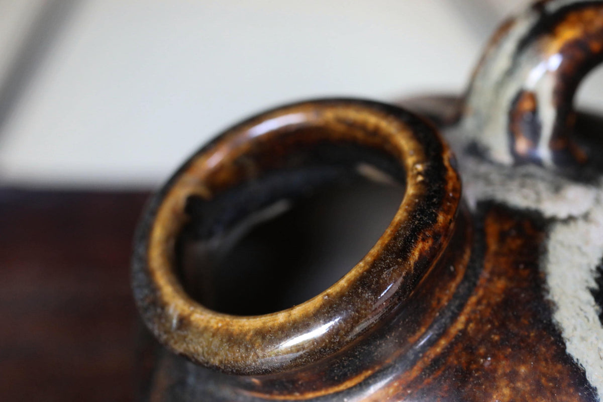 A close-up view of a ceramic vase with a brown and white glaze, featuring a large opening in the center.