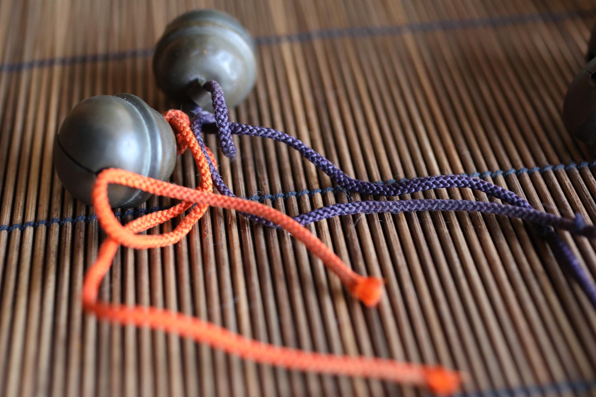 a pair of metal balls with orange and purple strings attached to them, resting on a bamboo mat.