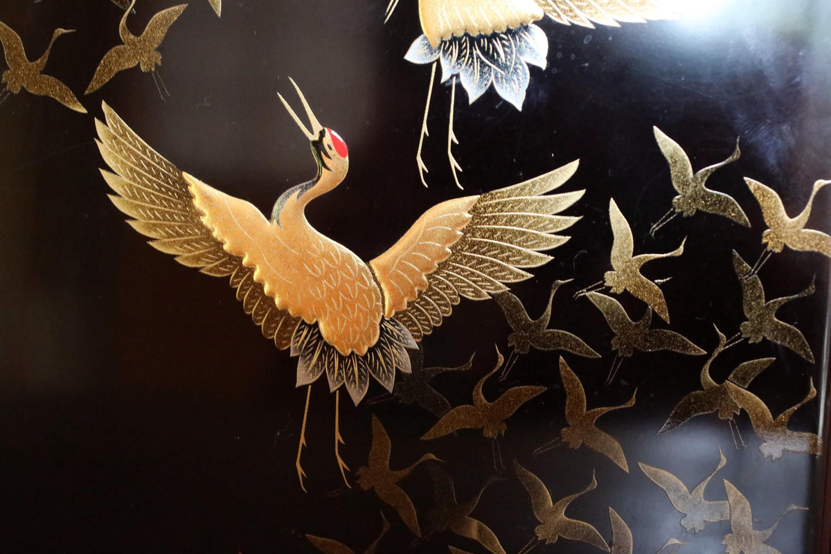 a close-up view of a detailed painting or artwork depicting a flock of golden cranes with outstretched wings against a dark background.