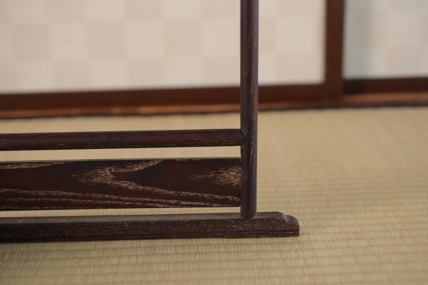 a close-up view of a wooden object, possibly a piece of furniture or a decorative item, with a blurred background that appears to be a room with a tatami mat floor.