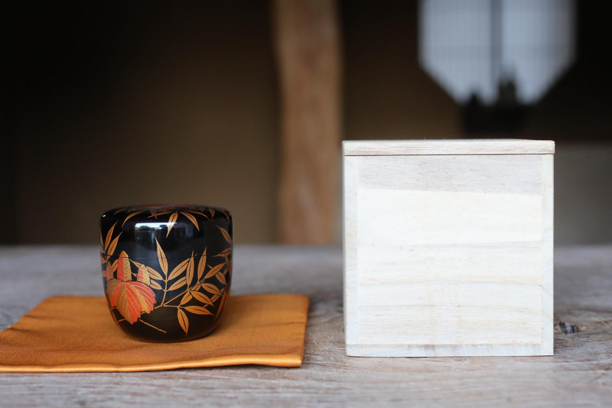 a black ceramic cup with a floral design and a white wooden box placed on a wooden surface.