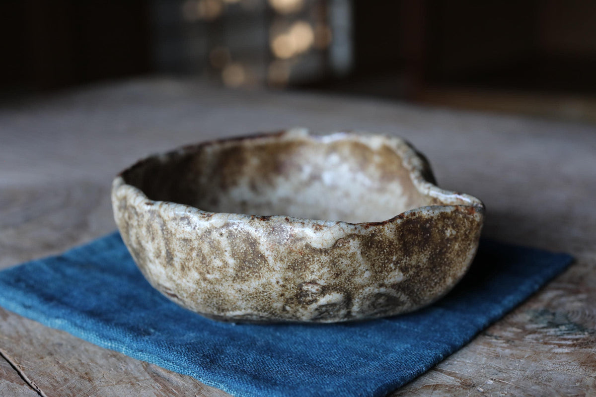 A ceramic bowl with a brown and white speckled pattern sits on a blue cloth on a wooden surface.