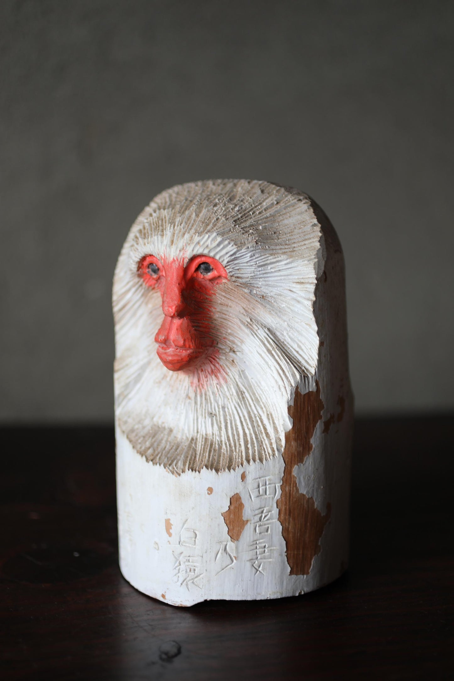 A wooden sculpture of a monkey's face with a red nose and white fur, sitting on a dark surface.