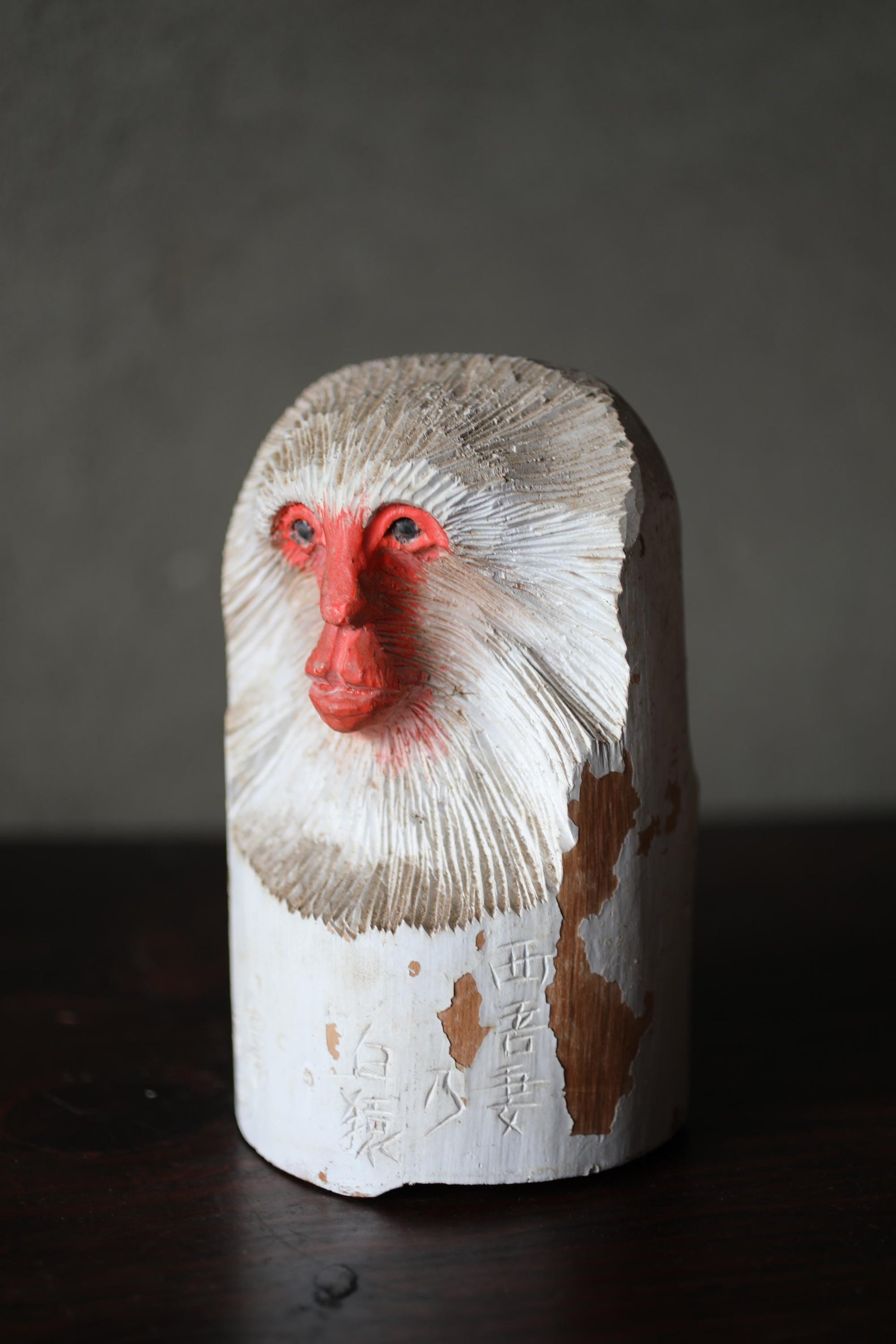 A wooden sculpture of a monkey's face with a red nose and white fur, sitting on a dark surface.