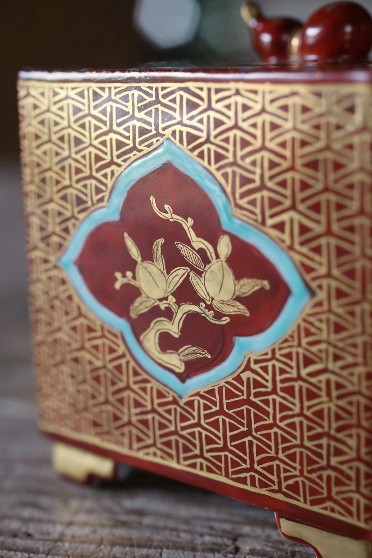 a close-up view of a decorative red and gold box with a floral design on the front.