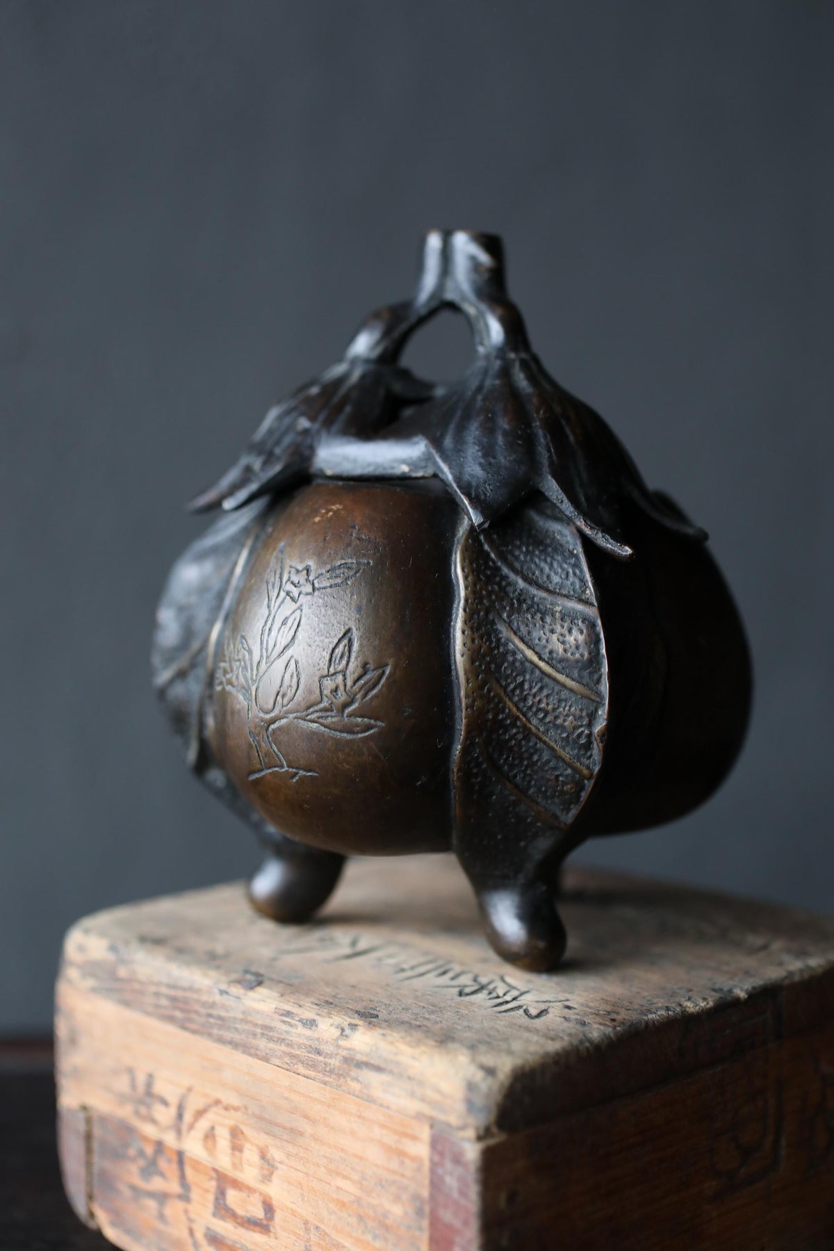 A bronze incense burner with a leaf design sits atop a wooden box with Chinese characters.
