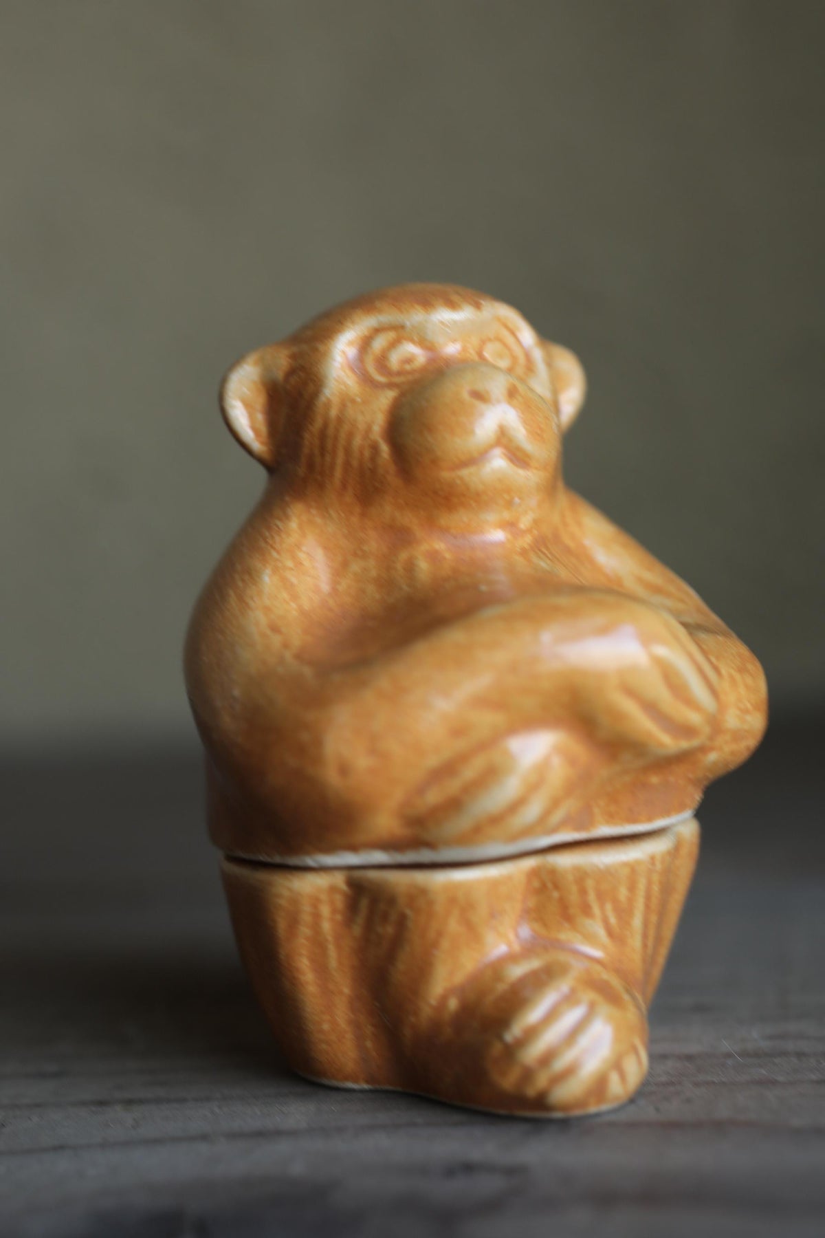 A ceramic figurine of a monkey sitting on a wooden surface.