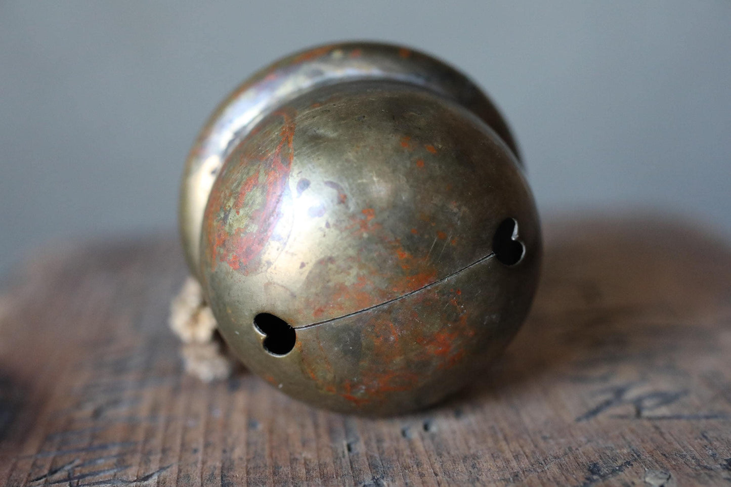 An old, rusted metal bell with a heart-shaped hole in the center, resting on a wooden surface.