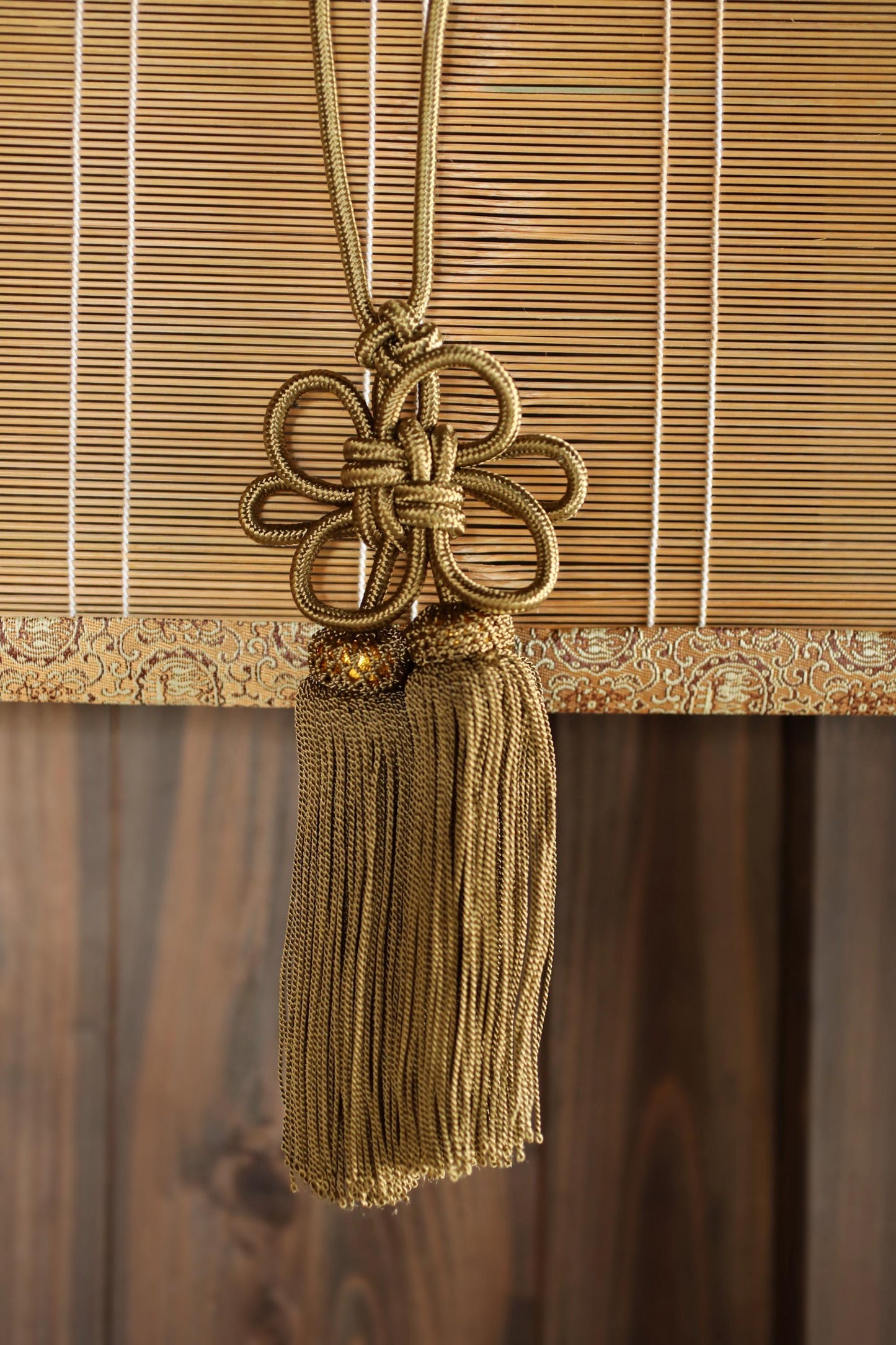 A gold-colored tassel hanging from a wooden blind, creating a decorative and elegant appearance.