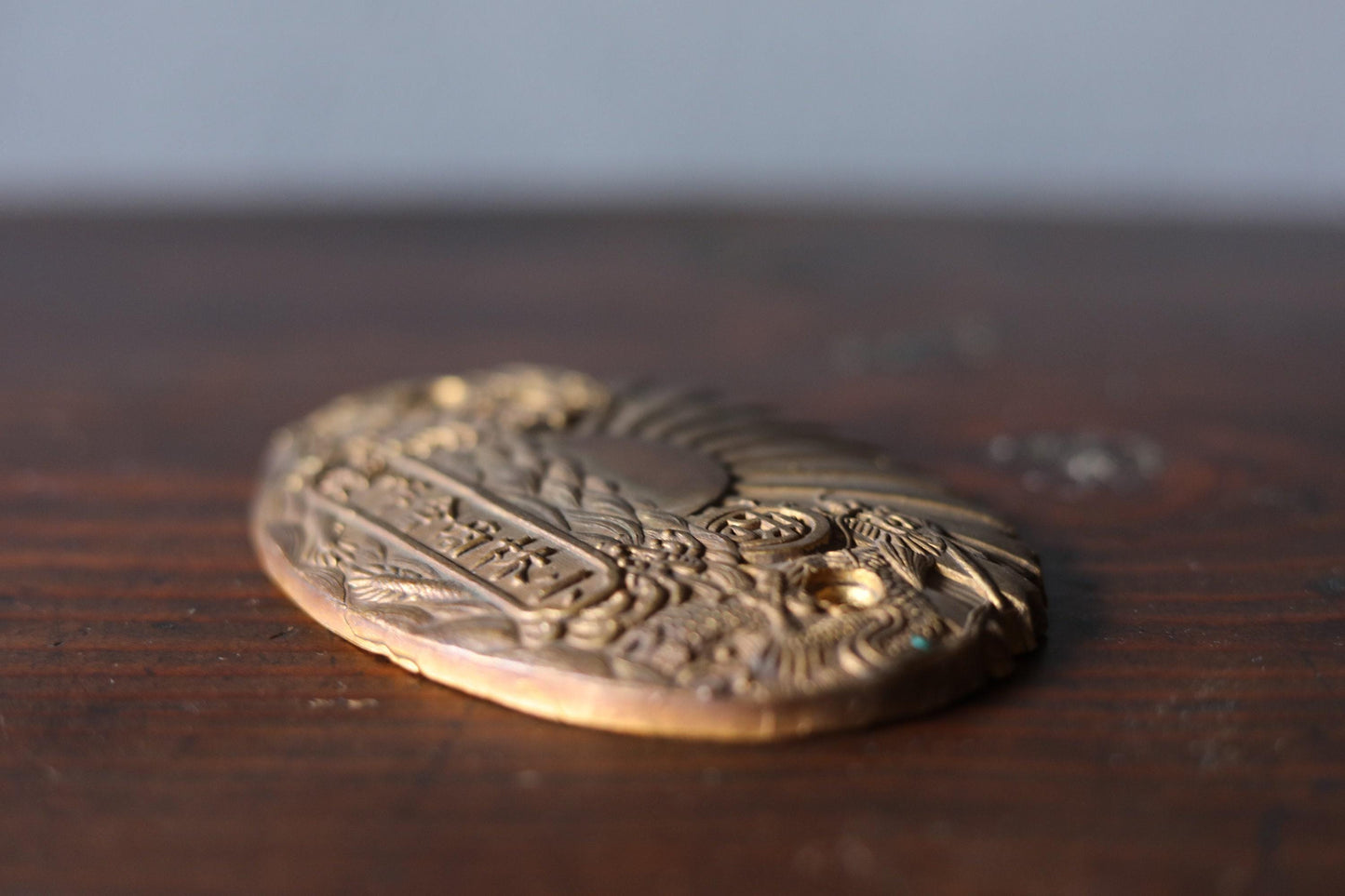 A close-up image of a decorative metal object, possibly a badge or plaque, resting on a wooden surface.