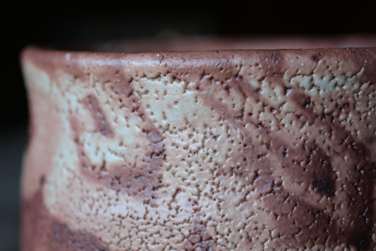 A close-up image of a textured ceramic object, possibly a vase or bowl, with a reddish-brown color and visible cracks and patterns.