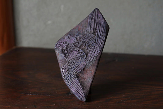A dark purple, diamond-shaped object with an intricate, embossed design on it, sitting on a wooden surface.