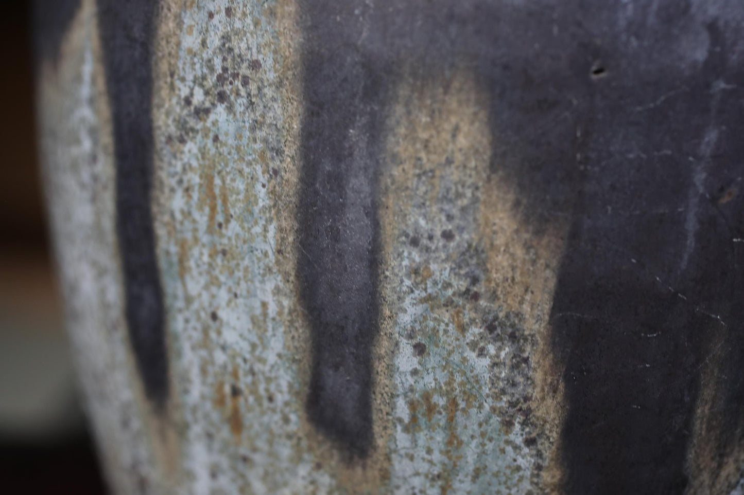 A close-up view of a textured ceramic or pottery surface, with a mix of dark and light colors, including shades of gray, black, and white.