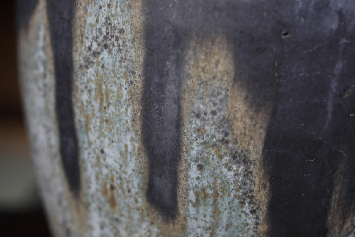 A close-up view of a textured ceramic or pottery surface, with a mix of dark and light colors, including shades of gray, black, and white.