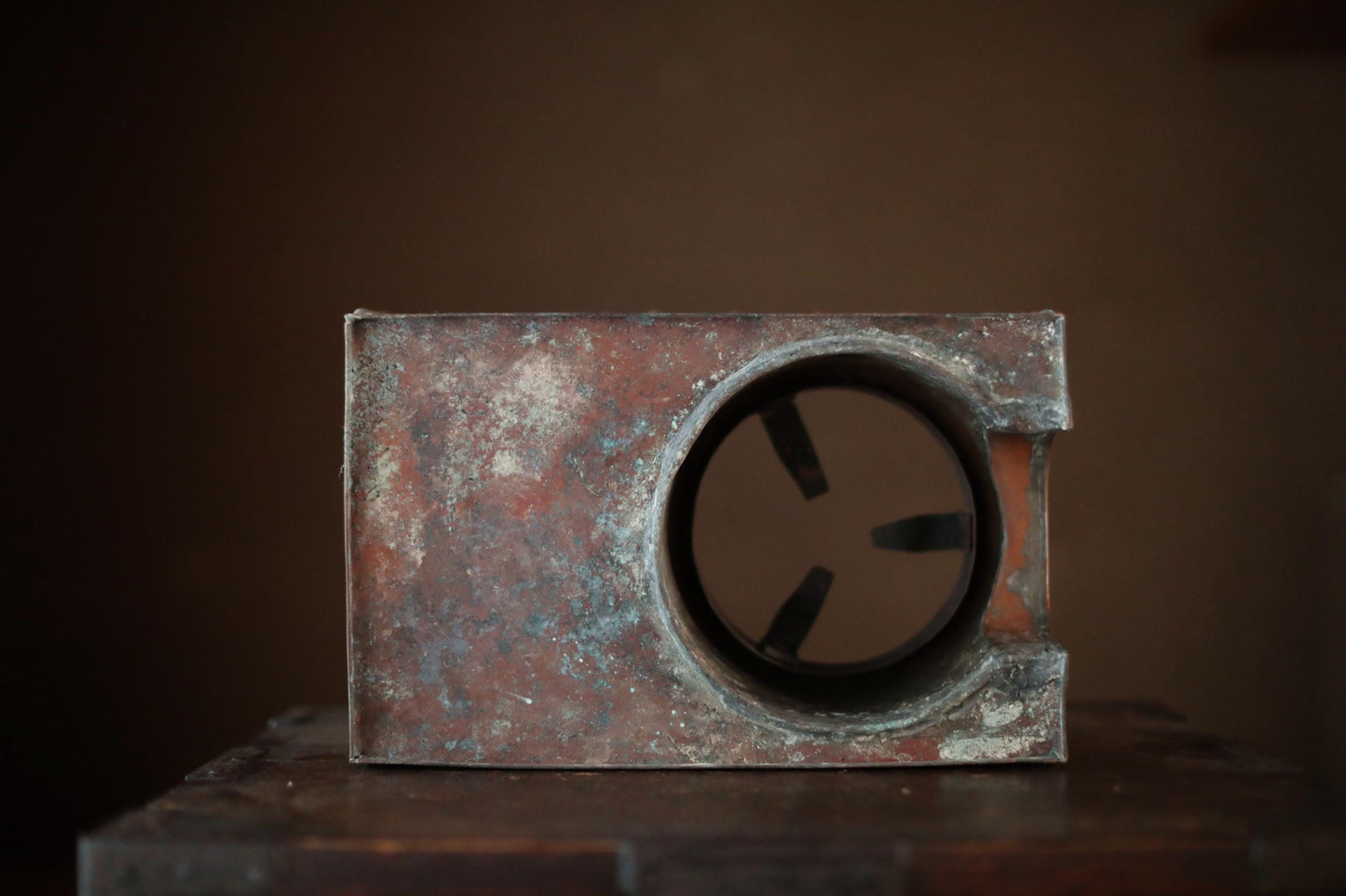a rusted metal object with a circular opening, sitting on a wooden surface against a dark background.